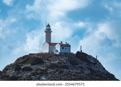 Rocky hilltop lighthouse with white walls and red roof under clear skies. - Powered by Shutterstock