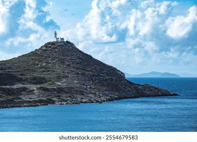 Rocky hilltop lighthouse with white walls and red roof under clear skies. - Powered by Shutterstock