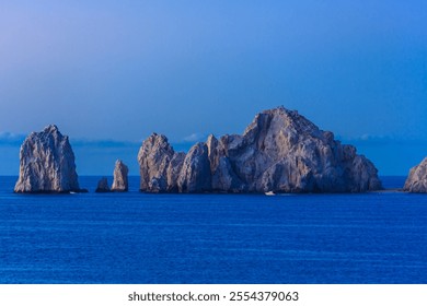 A rocky island with a blue ocean in the background. The sky is clear and the sun is setting - Powered by Shutterstock