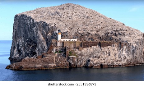 A rocky island with a white lighthouse and ancient fortifications surrounded by calm sea, under a clear blue sky. - Powered by Shutterstock