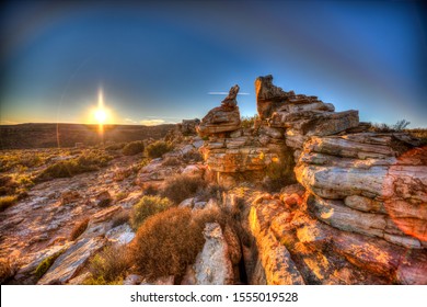 A rocky landscape in the morning with blue skies and the sun rising in the background.