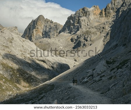 rocky landscape at the top of a natural park, hikers walking along a narrow path that leads to the top of a mountain, large rocky peaks and a feeling of grandeur