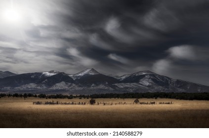 Rocky Mountain landscape scene during the winter with snow-capped peaks and a meadow in the foreground with a dramatic dark sky and wispy white clouds. - Shutterstock ID 2140588279
