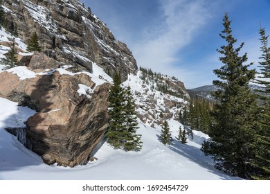 Rocky Mountain National Park Snowy Winter Landscape Of Rocky Cliff With Pine Trees And Blue Sky And Wispy Clouds