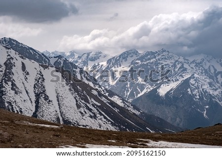 Rocky mountains covered with snow with storm clouds on background. Nature landscape. Scenic background. Bad weather in the mountains concept. Ancestral valley Sayram-Ugam National Park.