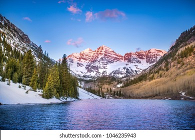 The Rocky Mountains near Aspen, Colorado glow in the light of the morning sunrise, as the mountains and trees reflect off the lake.