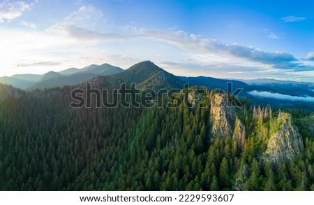Rocky peak of high mountain with vegetation in valley of Rhodope mountains and forests against background of sky with large clouds. Panorama, top view