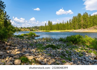 The rocky riverbank and shoreline of the Spokane River as it runs through the small town of Post Falls, Idaho, at McGuire Park.