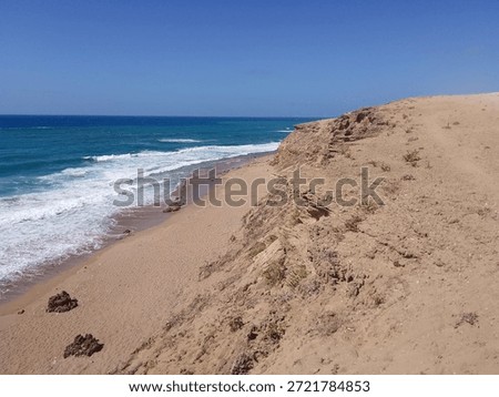 Rocky sandy beach with ocean waves and clear blue sky, natural coastline landscape.