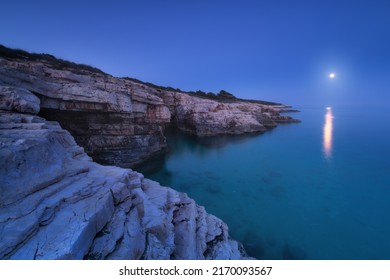 Rocky sea coast and full moon at night in summer. Beautiful landscape with beach, cliffs, stones in blurred water, cave, blue sky at twilight. Nature. Adriatic sea at night, Kamenjak, Croatia. Travel - Powered by Shutterstock