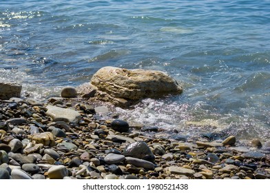 rocky sea shore with pebble beach, transparent waves with foam, on a warm summer day