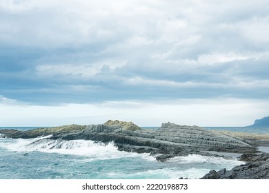 rocky seashore formed by columnar basalt against the backdrop of a stormy sea, coastal landscape of the Kuril Islands