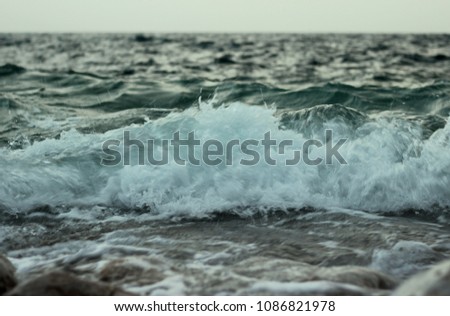 Rocky seashore with wavy sea and wind, waves crashing on the stones at Mediterranean coast area.