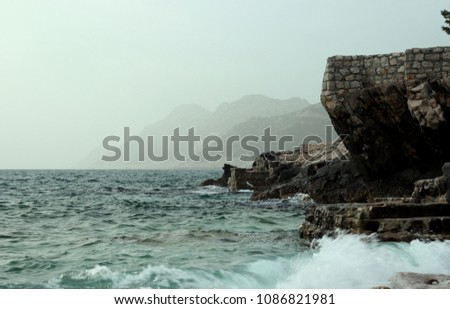 Rocky seashore with wavy sea and wind, waves crashing on the stones at Mediterranean coast area.