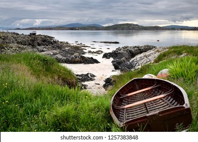 Rocky shore of Isle of Iona with beached boat with Fionnphort Isle of Mull and mountains of Ben More past Sound of Iona Inner Hebrides Scotland UK