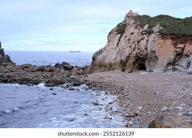 A rocky shoreline with a boat in the distance. The water is calm and the sky is overcast - Powered by Shutterstock