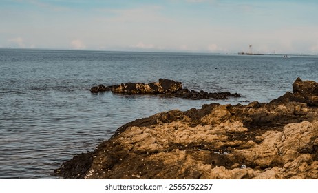 A rocky shoreline with a body of water in the background. The water is calm and the rocks are large and jagged. The scene is peaceful and serene, with the ocean - Powered by Shutterstock