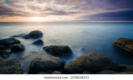 A rocky shoreline with a body of water in the background. The water is calm and the sky is cloudy - Powered by Shutterstock