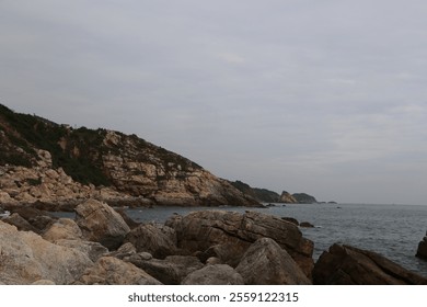 A rocky shoreline with a cloudy sky in the background. The rocks are scattered along the shoreline, and the water is calm - Powered by Shutterstock