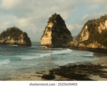 A rocky shoreline with a large rock formation in the distance. The water is calm and the sky is overcast - Powered by Shutterstock