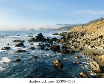 Rocky shoreline of the Oregon coast featuring clear blue water and incoming fog - Powered by Shutterstock