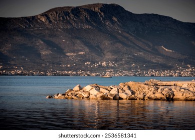 Rocky shoreline overlooking a calm sea with mountains in the background, under the warm light of a setting sun. The tranquil coastal scene captures the beauty of nature. - Powered by Shutterstock