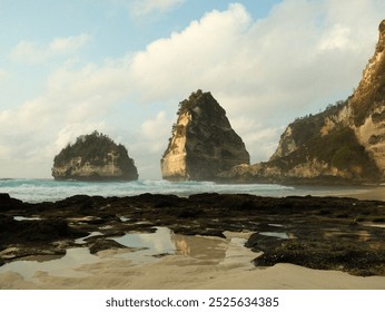 A rocky shoreline with a small body of water in front of a mountain range. The sky is cloudy and the water is calm - Powered by Shutterstock