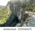 A rocky steep cliff covered with greenery on a sunny day in a walking trail at Nightcap National Park, Australia