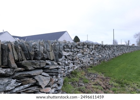Rocky stone wall separating grass and house