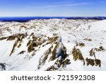 Rocky stones covered by moss and snow on top of Black Perisher mount in SNowy mountains national park of Australia during winter season overlooking snow covered mountain ranges around Perisher valley.