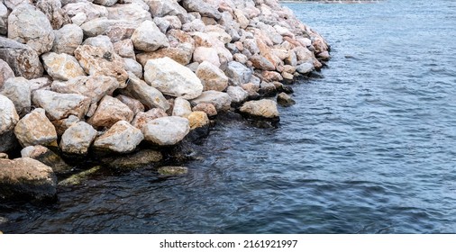 Rocky Wall Construction In Blue Ripple Sea. Rough Breakwater, Seawall Aged Build In Water Background. Summer Day, Seascape Concept.