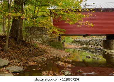 Roddy Road covered bridge is a majestic red color crossing over a stream. Autumn colors are turning in contrast to the red wood of the bridge near Thurmont MD.