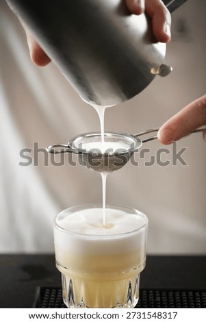 rofessional barman straining egg into cocktail glass for pineapple whisky sour. Shows attention to texture, aroma, and smooth foam creation