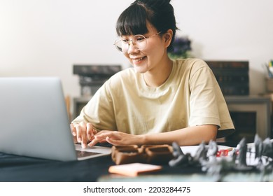 Role Playing Tabletop And Board Games Hobby Concept. Young Adult Asian Woman Using Laptop For Streaming Online With Friends. On Table With Blur Dice And Miniatures.