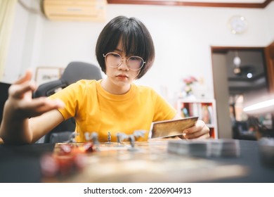 Role Playing Tabletop And Board Games Hobby Concept. Young Adult Asian Woman Enjoying With Storytelling. Blur Foreground With Monster Miniatures And Dice Component.