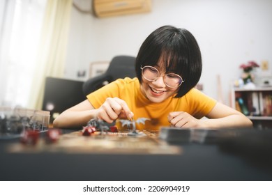 Role Playing Tabletop And Board Games Hobby Concept. Young Adult Asian Woman Enjoying With Storytelling. Blur Foreground With Monster Miniatures And Dice Component.