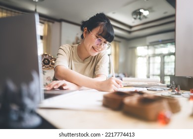 Role Playing Tabletop And Board Games Hobby Concept. Young Adult Asian Woman Using Laptop For Streaming Online With Friends. On Table With Blur Dice And Miniatures.