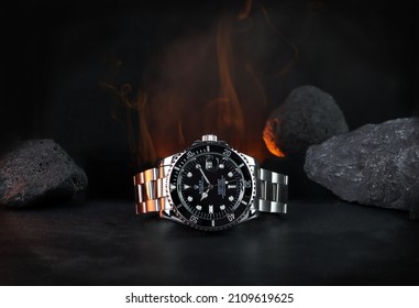 The Rolex Vintage Wristwatch Ceramic Bezel Model Black Oyster Perpetual Submariner Date 39 Mm Display On Black Table With Background Of Flame And Rocks In The Dark Shelf Of Luxury Watch Exhibition