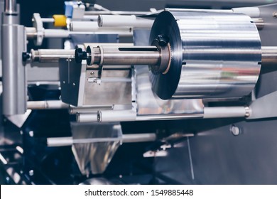 Roll Of Aluminum Foil For Food Packaging On The Automatic Packing Machine In Food Product Factory. Industrial And Technology Concept. 