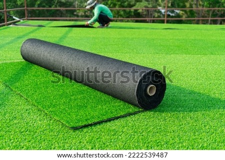 Roll of an artificial turf laying background. A synthenic grass layer. Greenering of the yard of , green lawn background with workers pave the counterfeit grass.