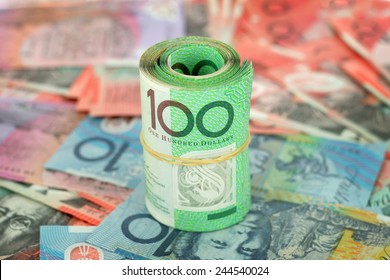 A roll of Australian $100 notes on a background of notes