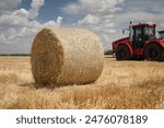 A roll of dry hay lies in a field after harvesting against the background of a tractor. The end of the agricultural season.