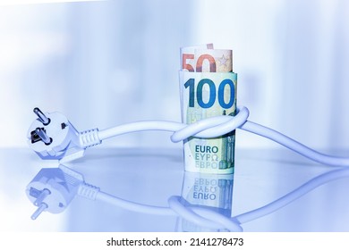 Roll Of Euro Banknotes Tied With An Electrical Plug On Light Background. Concept Of Saving Electricity At Home. Electricity Cost And Expensive Energy Concept. Electricity Consumption  