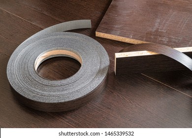 Roll melamine edge for finishing of furniture. Edging tape lying on laminated chipboard sheets wenge color. - Shutterstock ID 1465339532