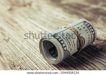 Roll of One Hundred Dollars bill on a wooden table. Cash Money American Dollars. Close-up view of stack of US dollars.