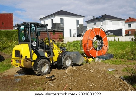 Roll of orange fiber optic cable for faster Internet in rural regions. Yellow digger for laying the underground cable in the soil. Barsinghausen, district of Hanover, Germany.                