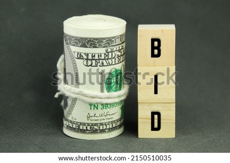 a roll of paper money and a wooden cube with the word bid concept