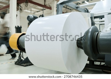Roll of polymer material set on flexographic printing press, unrecognizable worker walking on background