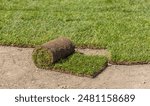 A roll of sod, partially unrolled, sits on bare ground, revealing the lush green grass underneath. It is ready for landscaping and installation.