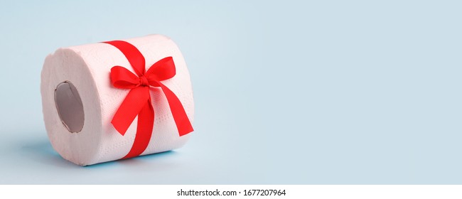 Roll Of Toilet Paper Wrapped In Gift Bow. The Concept Of A Valuable Actual Gift, A Meme On The Deficit In Supermarkets, Coronavirus Covid-19, Panic, Excitement And Shortage Of Goods, Banner